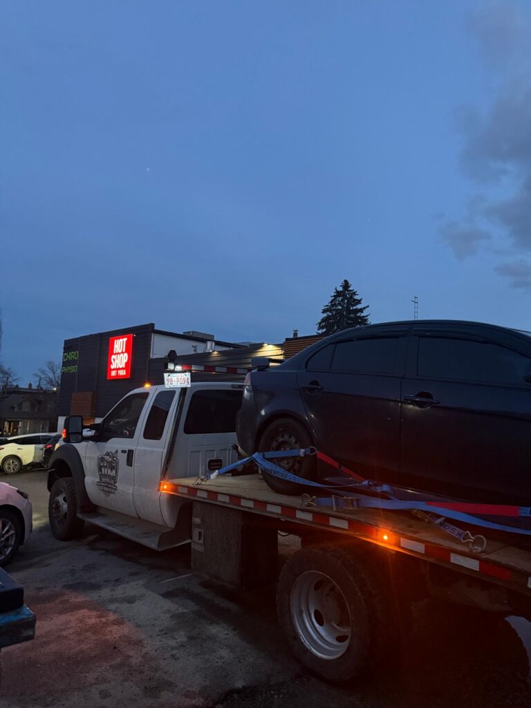Jim Towing flatbed loading a vehicle at dusk in Calgary