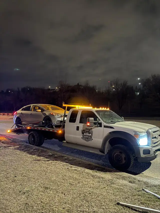 Jim Towing flatbed with a sedan loaded at night
