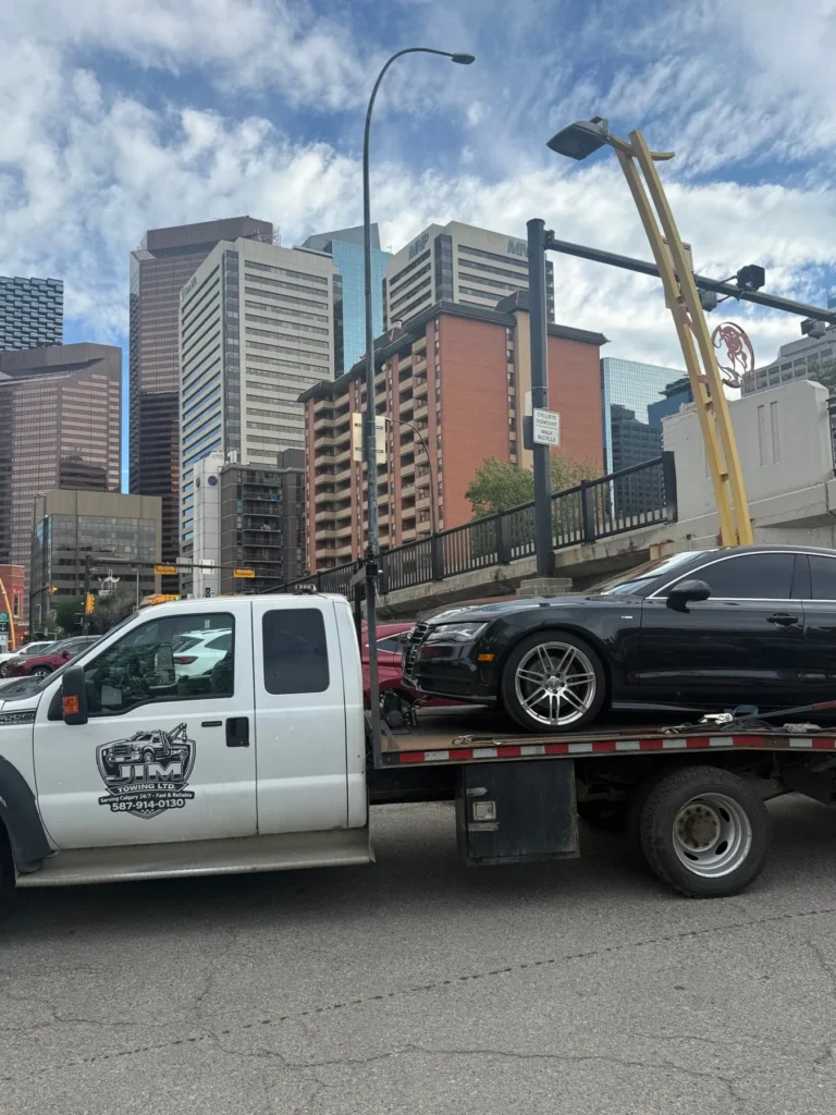 Jim Towing flatbed carrying a black sedan in downtown Calgary
