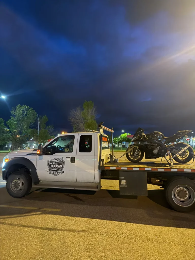Jim Towing flatbed truck transporting a motorcycle at night