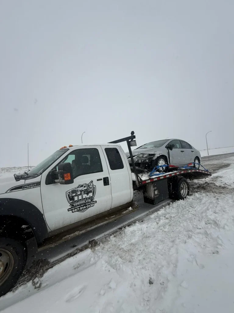 Jim Towing flatbed recovering a sedan on a snowy Calgary road